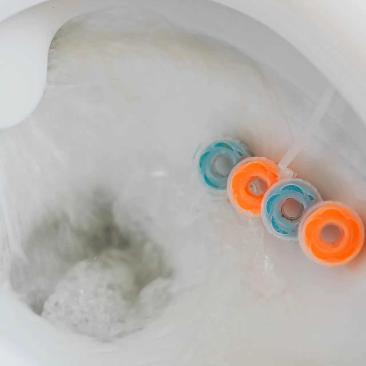 Toilet flushing with water and a blue and orange block freshener